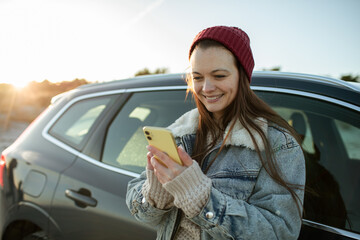 Young adult woman using a smart phone next to her car on a beach