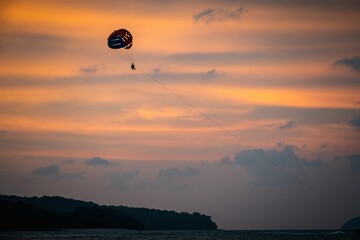Distant shot of a paraglider with a parachute against the golden sky at sunset