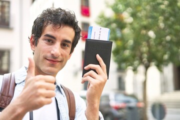 Excited young man proudly displays his airplane tickets while enjoying a vacation in a new and vibrant city.