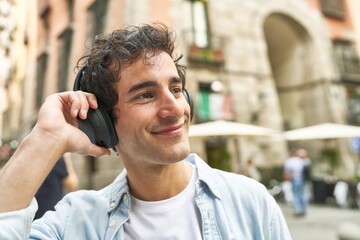 Young man finds joy and inspiration in the rhythm of his music, sporting headphones and a cheerful expression as he moves through the city.