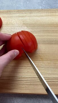 Vertical screen: Cook cuts tomato with a large kitchen knife. utting tomatoes while cooking vegetable fresh salad on table. Preparing food. Healthy eating. Sliced tomato. Keto or paleo diet, close up