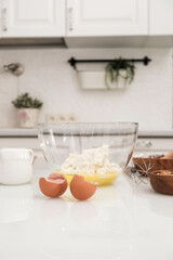 Fototapeta na wymiar Ingredients for baking: eggs in glass bowl, flour, cottage, milk, nuts in light kitchen.