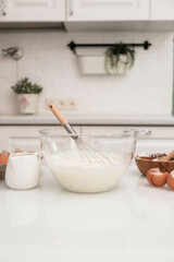 Ingredients for baking and dough: eggs in glass bowl, flour, cottage, milk, nuts in light kitchen.