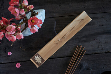 Burning japanese incense stick on wooden incense holder and vase with flowering chinese quince...