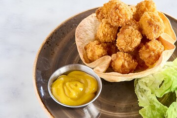 Top view of crispy popcorn chicken served with a sauce and lettuce