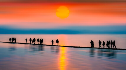 silhouettes of people walking on the beach at sunset
