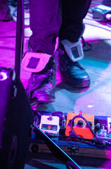 A guitar musician playing a wah wah effects pedal on stage at a concert with purple lighting