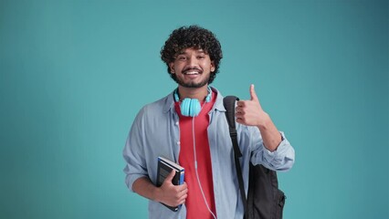 Smiling happy young adult arab or indian man student standing isolated on blue background, showing thumbs up like hand gesture giving recommendation advertising good service or result.