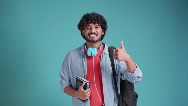 Smiling happy young adult arab or indian man student standing isolated on blue background, showing thumbs up like hand gesture giving recommendation advertising good service or result. - Powered by Adobe