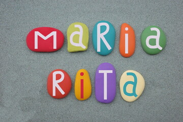 Maria Rita, female given name composed with multi colored stone letters over green sand