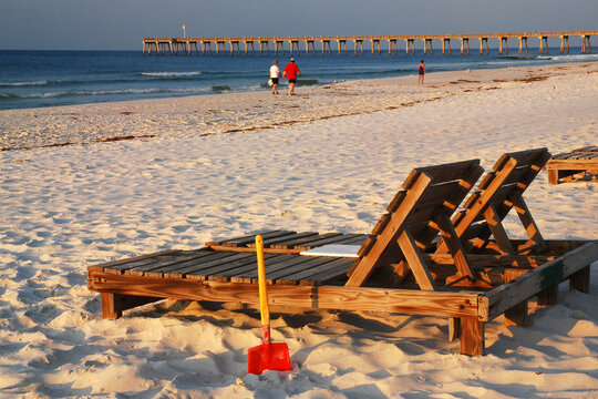A wooden lounge chair awaits relaxation seekers in on the sand of the beach of the Gulf of Mexico