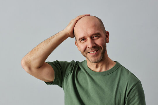 Portrait of mature bald man smiling at camera and posing confidently with hand on head, copy space