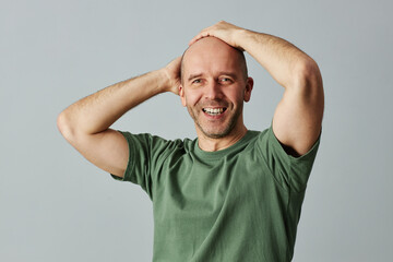 Waist up portrait of confident bald man smiling at camera and posing with hands on head