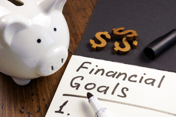 Piggy bank and open notepad with inscription financial goals and list.
