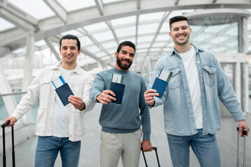 Group Of Cheerful Male Tourists Showing Boarding Passes In Airport