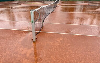 Wet clay tennis court with puddles during the rain. Outdoor tennis season. Spring rain on courts. All practices and match are cancelled! ccourts