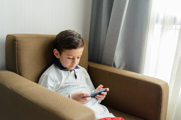 Child sitting in an armchair playing with a smartphone.