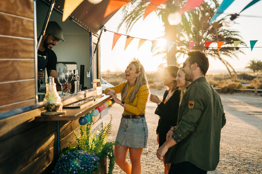 Joyful friends laughing with barman near food truck