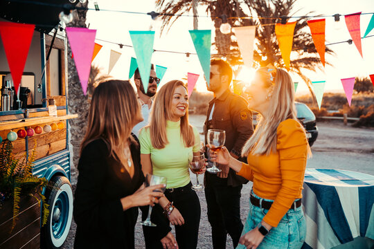 Happy women with wineglasses chatting near men on beach