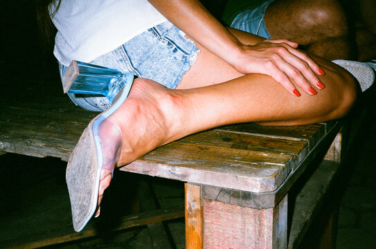 Anonymous woman sitting wooden pallet wearing plastic high heels party
