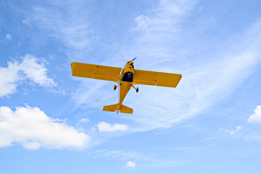 Yellow single-engine ultralight airplane flying in the blue sky with white clouds