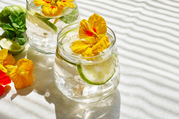 Iced lemonade with edible nasturtium flowers, lime and mint leaves. Refreshing summer drink. Healthy organic summer soda drink. Detox water. Diet unalcolic coctail.