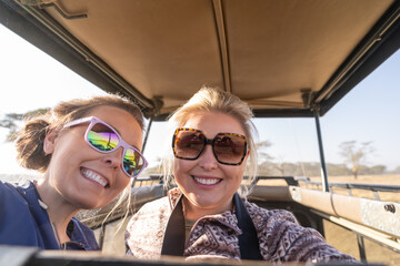 Two women on safari take a selfie out of the rooftop vehicle, in Kenya, Africa