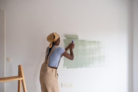 African American woman painting wall with effort