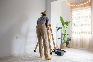 Black painter putting ladder near wall
