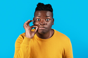 Keep Quiet. Young Black Man Making Zipping Mouth Gesture Over Blue Background