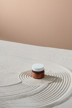 Skincare product package in glass jar on fine sand.