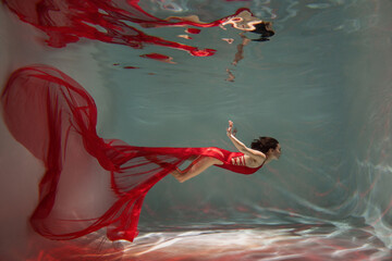 Graceful lady in scarlet dress posing underwater