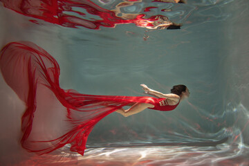 Graceful lady in scarlet dress posing underwater