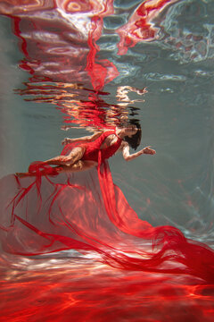 Graceful lady in scarlet dress posing underwater