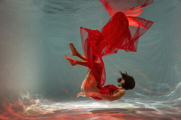 Graceful lady in scarlet dress posing underwater