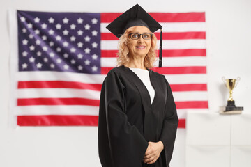 Marture woman wearing a graduate gown and posing in front of USA flag