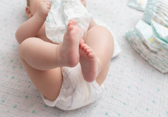 A baby in a diaper lies on a white background plays with a stack of diapers. Copy space for text