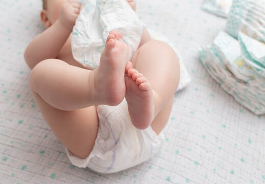 A baby in a diaper lies on a white background plays with a stack of diapers. Copy space for text