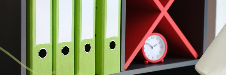Shelf with office folders with documents and alarm-clock