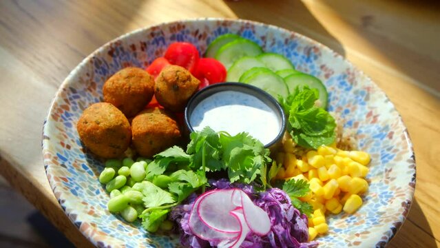 Chickpea falafel salad with vegetables, quinoa and Edamame beans with Zaziki sauce on a wooden table. Healthy vegetarian food. High quality 4k footage. Bright, juicy fresh rations. Healthy lifestyle