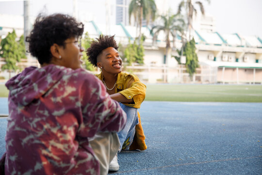 Two smiling men looking aside while sitting down and relaxing at park