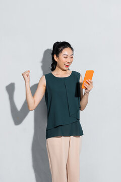 Asian woman smile broadly while looking at phone in hand and raise