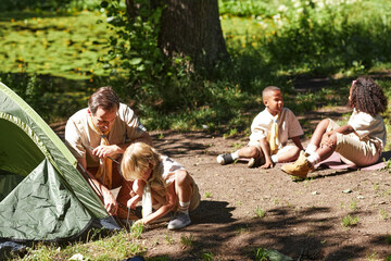 Group of scouts setting tent during hiking trip in forest scene lit by sunlight