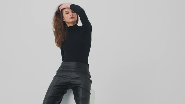Portrait of a young sexy fashion model dressed in black standing and isolated over white background. Woman looking at camera. 4k. Slow motion