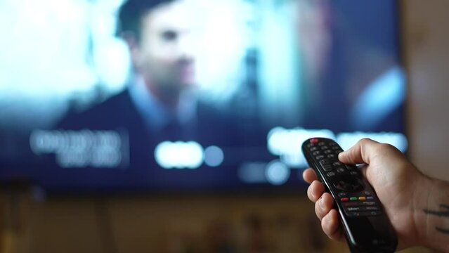 Hand holding the remote control on the background of the TV and scrolling through the channels