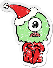 distressed sticker cartoon of a cyclops alien spaceman wearing santa hat