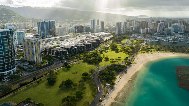 Aerial top view from above of Honolulu Hawaii cityscape with green park area and blue ocean at sunrise with lightrays and cloud shadows 