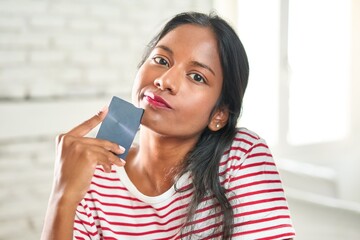 Thoughtful young Indian woman holding credit card