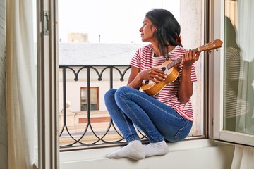 Indian woman playing ukulele on windowsill