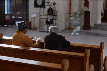 Rear view of mature woman talking to priest while reading Bible in church